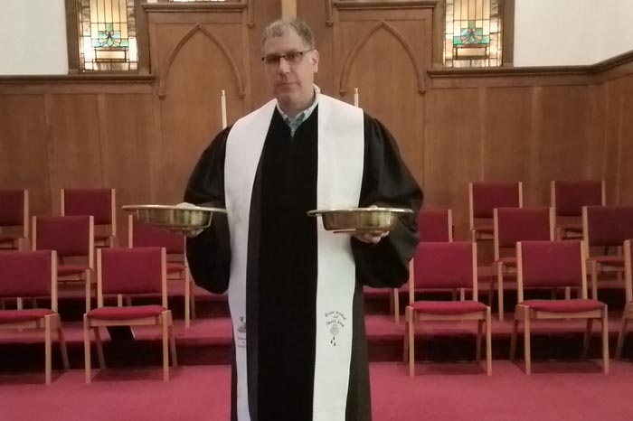 While the Rev. Richard Burstall promotes the availability of online giving at Michelson Memorial United Methodist Church, receiving gifts in the traditional plates is still a part of each service. Photo courtesy of the Rev. Richard Burstall. 