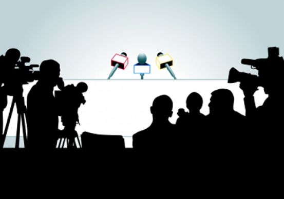 silhouettes of media in front of interview desk with microphones