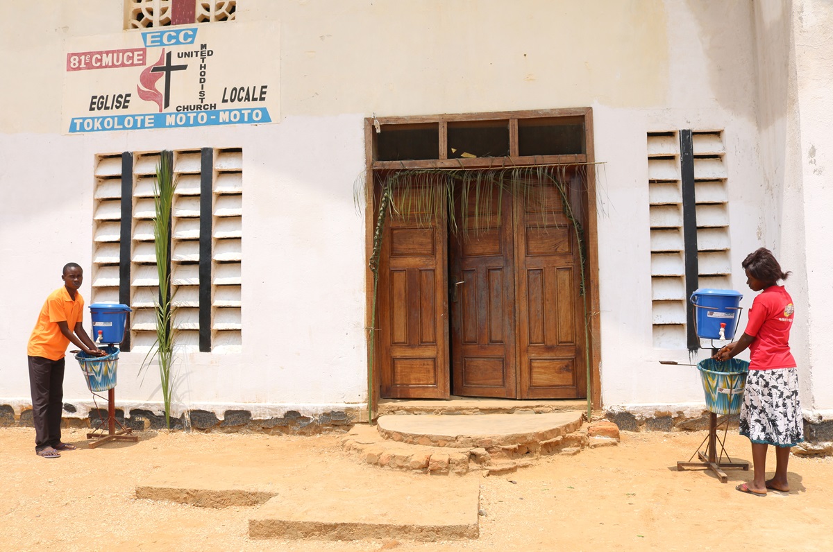 Two worshippers wash their hands using handwashing kits installed in front of the Tokolote MotoMoto United Methodist Church in the Kindu Nord District. The United Methodist Board of Global Ministries funded the installation of the handwashing stations at local churches in the Eastern Congo Episcopal Area. Photo by Chadrack Tambwe Londe, UMNS.