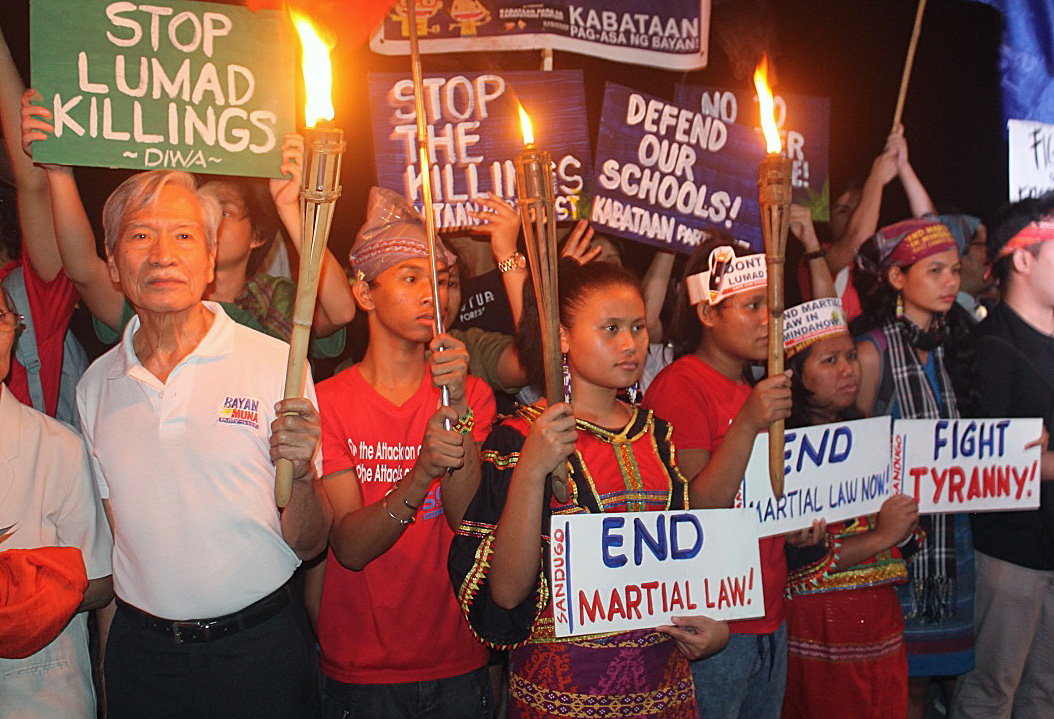 Participants hold signs during an interfaith gathering at Rajah Sulayman plaza in Manila. Satur Ocampo (left), a well-known social activist, commended the interfaith initiative, calling it “a signal that society should not remain silent in the face of such exigencies.” Photo by Gladys Mangiduyo, UMNS.