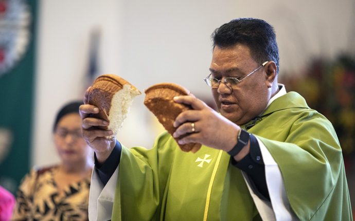 The Rev. Tevita Ofahengaue breaks the Communion bread during a service that features both the English and Tongan languages. In the background is Christiana Uesi.