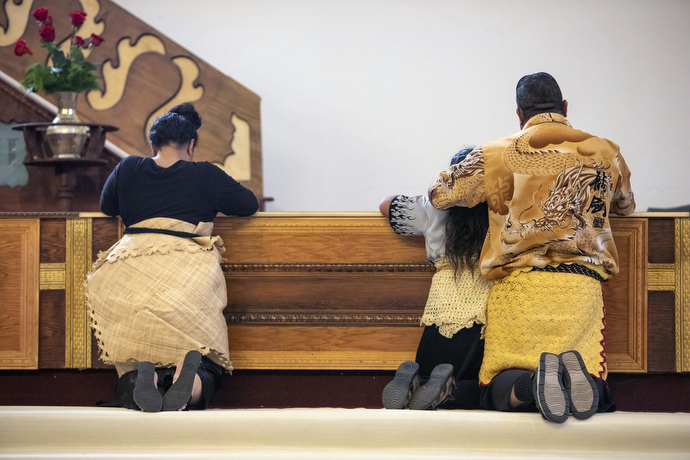 Afu Molisi Jr. prays with his family after receiving communion. Like many in the congregation, he wears the traditional dress featuring the kie kie waist tie as a sign of respect. 