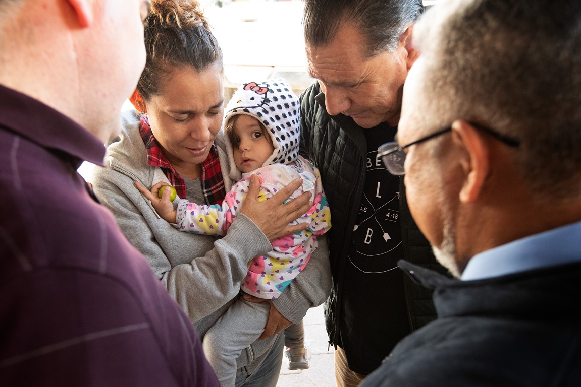 The Rev. Arturo Gonzélez Sandouzl (second from right) and other members of the United Methodist Immigration Task Force pray with Isabél and her 16-month-old daughter Kassandra at a makeshift camp near the bridge leading to the U.S. in Matamoros, Mexico. The mother and daughter traveled from Nicaragua in hopes of seeking asylum in the U.S. Photo by Mike DuBose, UMNS.