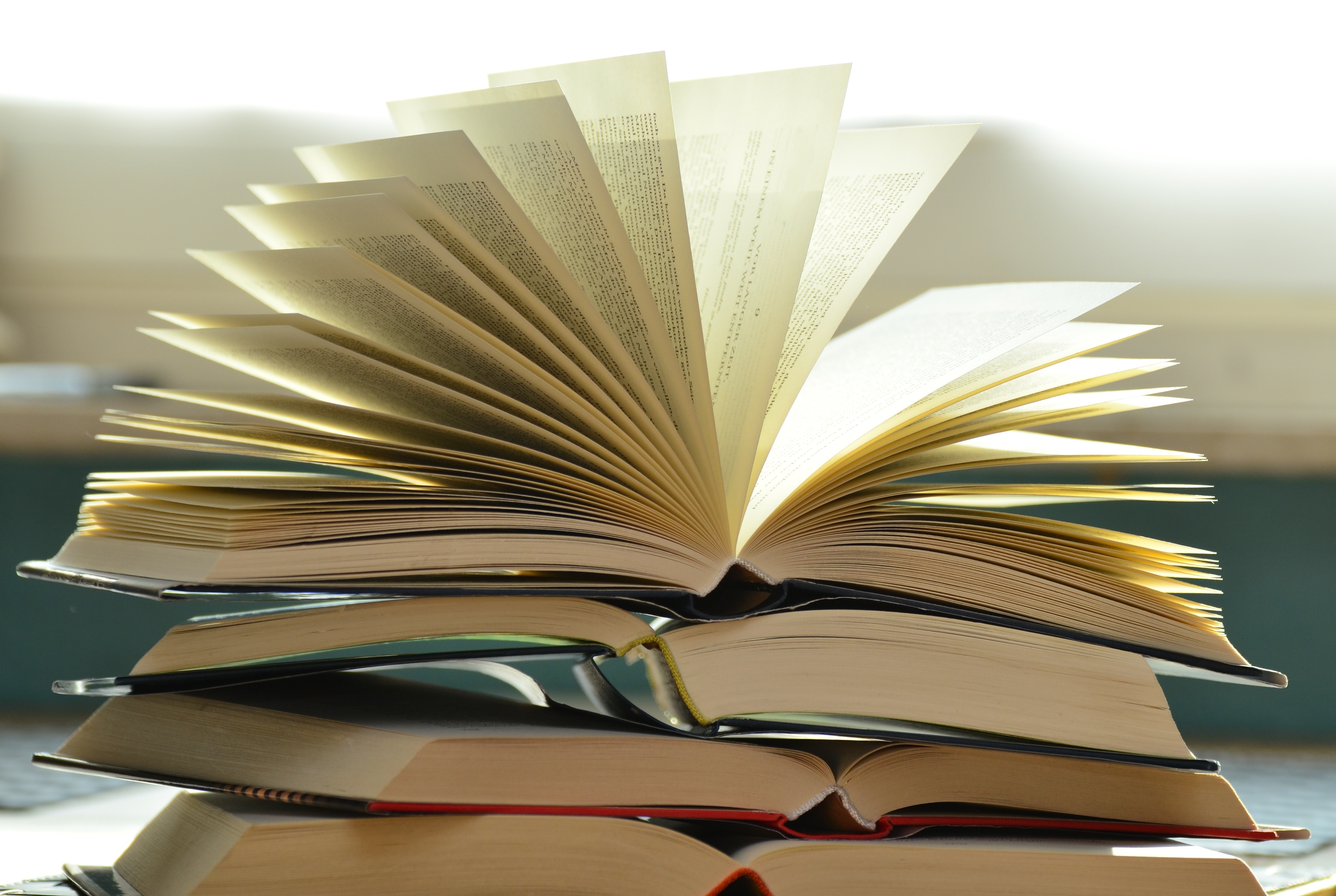 A stack of open books with a blurred background. Photo from Pixabay via Pexels.com.