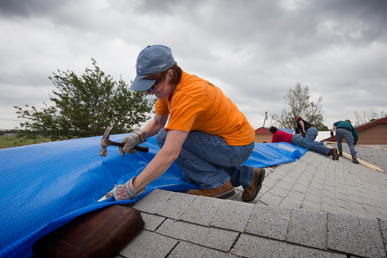 Kaci Underwood works to fasten down a tarp over a tornado-damaged roof in advance of a brewing storm in Moore, Okla. Underwood was part of a volunteer team working out of First United Methodist Church in Moore. Photo by Mike DuBose, UMNS.
