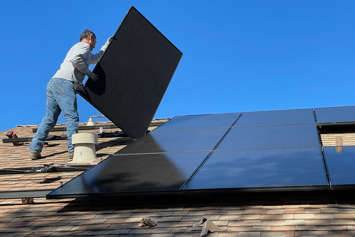 A man installs solar panels on a roof. Image by Bill Mead, Unsplash.com.