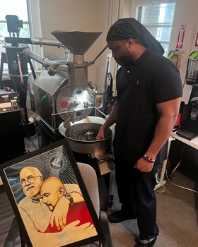 Timothy “GA” Underwood roasts coffee beans next to a painting of Father Greg Boyle, who inspired Deep Time's social enterprise, at Deep Time Asheville. You can support the ministry by ordering a bag of coffee. Courtesy of Luke Edwards