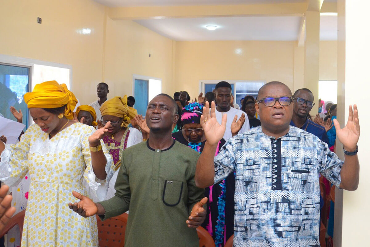 (From left) Naoutane Ndecky, Senegal District women’s president, Abraham Basse, district lay president, and Eric Ané raise their hands in prayer during the dedication service at Temple Beth Shalom United Methodist Church in Diamniadio, Senegal. The ceremony marked the official inauguration of the new modern building, the result of a collective effort to provide United Methodists in the community with their own place of worship after 18 years of renting. Photo courtesy of the Senegal District.