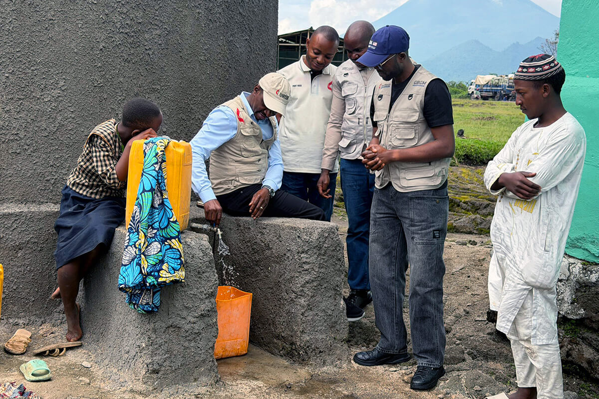 Jean Tshomba, coordinator of the United Methodist Committee on Relief’s Disaster Management Office in Eastern Congo, turns on the tap of a new rainwater cistern in Kibumba, Congo, as Dr. Damas Lushima (wearing a blue hat), team members and a young girl from the village look on. With funding from UMCOR, 24 rainwater collection tanks were installed to  provide vital access to safe drinking water in this remote village, which is devoid of surface water sources and weakened by recent population displacements. Photo by Jolie Shabani, UM News.