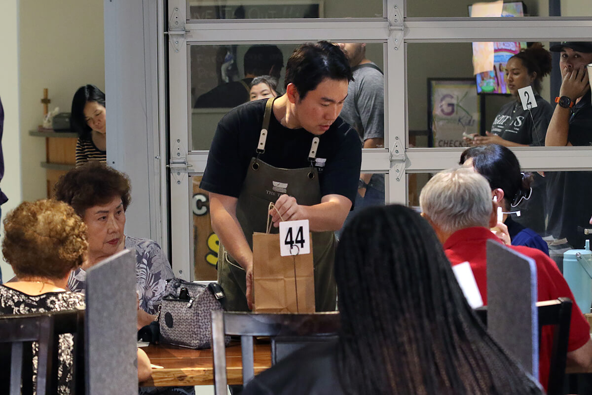 The Rev. Changhyun Kim, pastor of Bonfire United Methodist Church and chef at The Table Korean Cuisine in Olathe, Kan., talks with customers as he delivers a takeout meal to a table during Friday dinner service. Kim has turned his passion for his native cuisine into a successful outreach ministry for Bonfire, a new congregation supported by the Great Plains Conference’s church development ministry. Photo by the Rev. Thomas E. Kim, UM News.