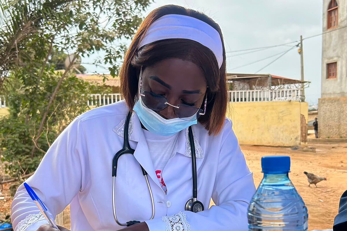 Dra. Rosa Manuel, num consultório médico improvisado no quintal da Igreja Metodista Unida de Luis Correia Kizembe em Luanda fazendo a prescrição médica de uma paciente no seu programa social de assistência médica e medicamentosa. Foto cortesia de Orlando da Cruz, Notícias MU.