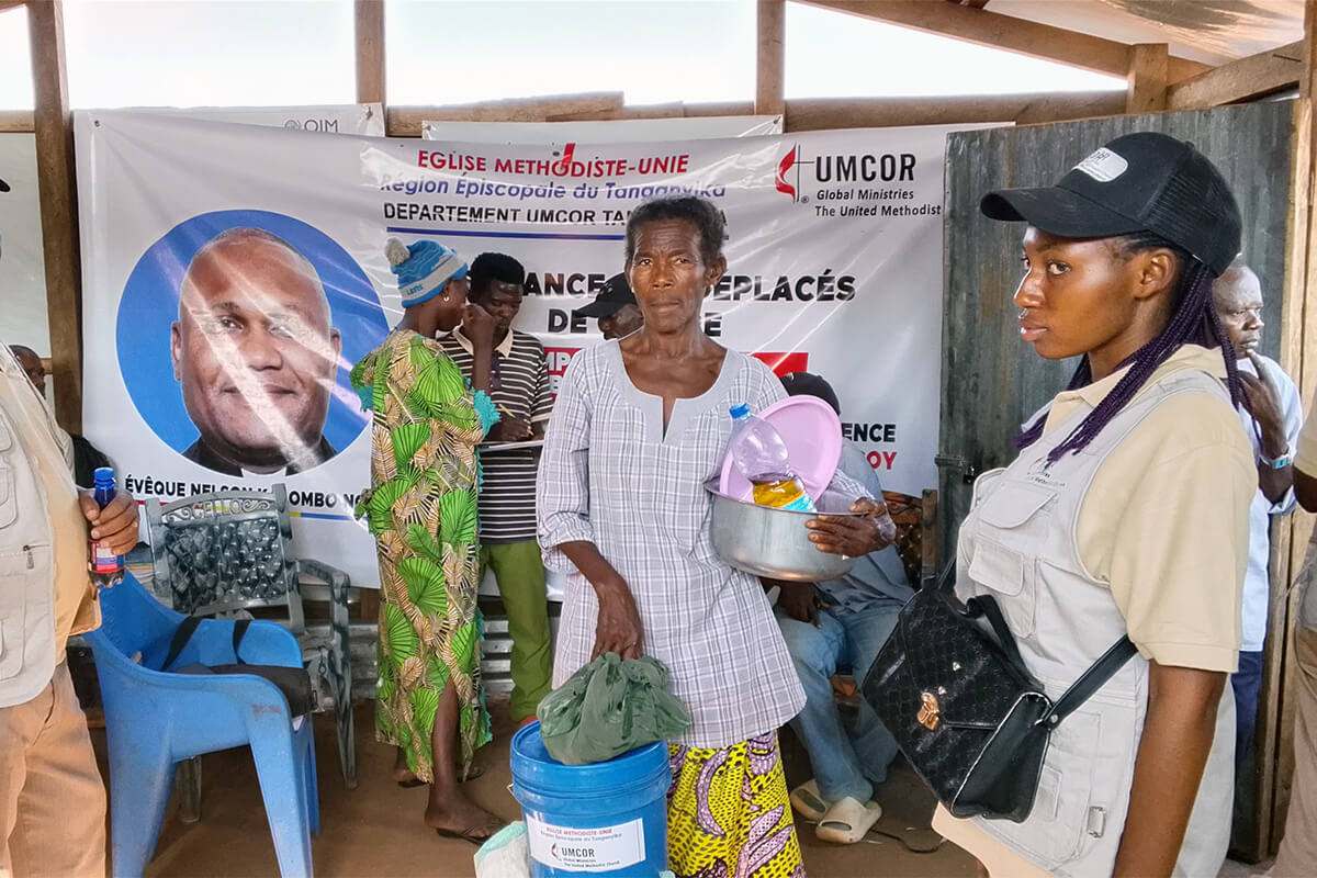 Mwavita Ndjali (au centre) reçoit son kit d’articles alimentaires et non alimentaires sur le site de Mushaba, près de Kalemie, au Congo, en présence d’une équipe du Bureau de gestion des catastrophes de l’UMCOR de la Région épiscopale du Tanganyika. L’aide d’urgence, financée par une subvention de près de 50 000 dollars de l’UMCOR, apporte un soulagement vital à 704 ménages qui ont fui les violences armées au Kivu. Photo de Mpyana Wa Kasongo M. Pascal, UM News.